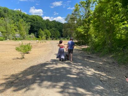 A woman and a man walking down the path at the park with their dog