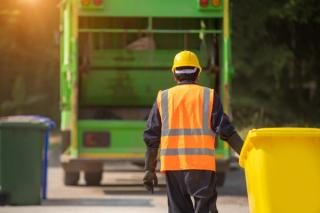Waste collector pulling yellow bin to a bin lorry to be emptied. 