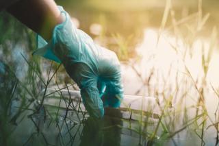 Gloved hand collecting water sample with test tube